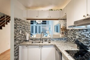 A modern kitchen with a granite countertop, stainless steel sink, and a black stove. - Oceanside Golf and Resort Villa in Dorado (Dorado)