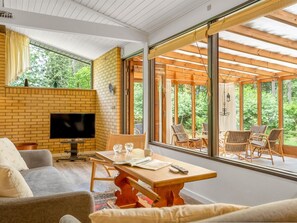 Ein modernes Wohnzimmer mit Backsteinwand, Flachbildfernseher, Holztisch und Korbstühlen.
