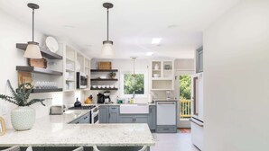 Una cocina moderna con gabinetes blancos, encimera de mármol e iluminación colgante.