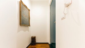 Un pasillo estrecho con suelo de madera, un cuadro enmarcado en la pared y un teléfono fijado a la pared.