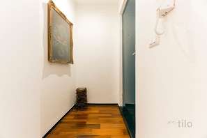 Ein schmaler Flur mit Holzboden, einem gerahmten Kunstwerk an der Wand und einem an der Wand befestigten Telefon.