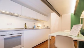 Eine kleine Küche mit weißen Schränken, einem eingebauten Backofen, einem Tisch mit einem Stuhl und einer Wand in Grünton.