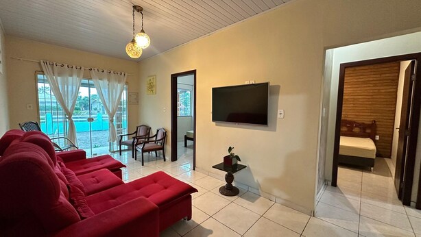 Una sala de estar con televisor, sofás rojos, una mesita y vistas por una ventana.