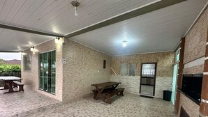 Un patio al aire libre con una mesa y bancos de madera, un refrigerador y una puerta de cristal que da a un jardín.