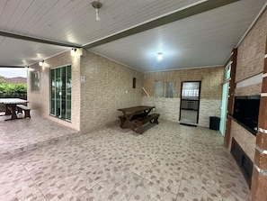 An outdoor patio area with a wooden table and benches, a refrigerator, and a glass door leading to a garden. - casa grande praia da pinheira (Palhoça)