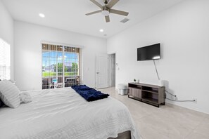 Un dormitorio con cama, ventilador de techo, televisión y balcón con vistas.