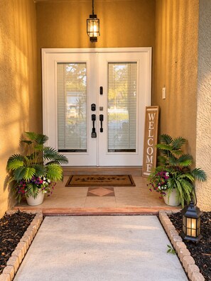 A front door with a 'WELCOME' sign, two potted plants, a doormat, and a lantern. - 4BR  Private Pool, Game Room & Sleeps 10 (Spring Hill)