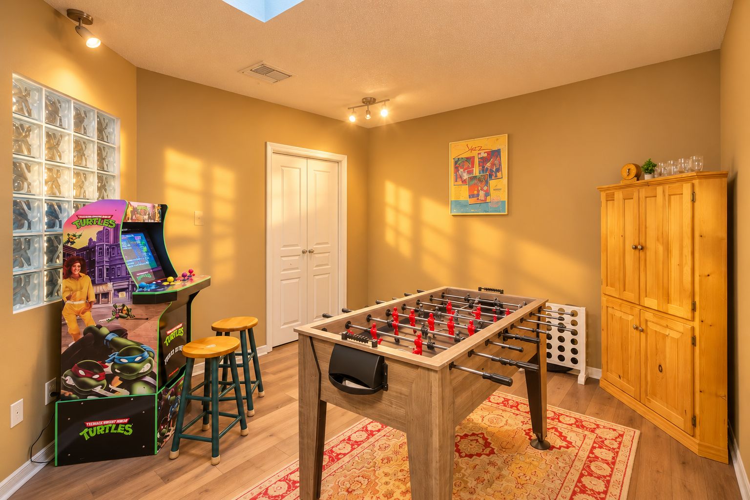 Una habitación con una mesa de fútbol de mesa, un taburete para jugar al fútbol de mesa, un armario y una máquina de juegos instalada en la pared.