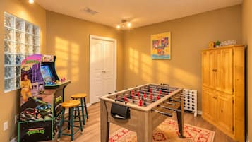Una habitación con una mesa de fútbol de mesa, un taburete para jugar al fútbol de mesa, un armario y una máquina de juegos instalada en la pared.
