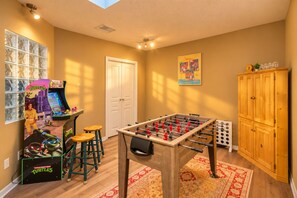 A room with a foosball table, a foosball stool, a cabinet, and a wall-mounted game machine. - 4BR  Private Pool, Game Room & Sleeps 10 (Spring Hill)