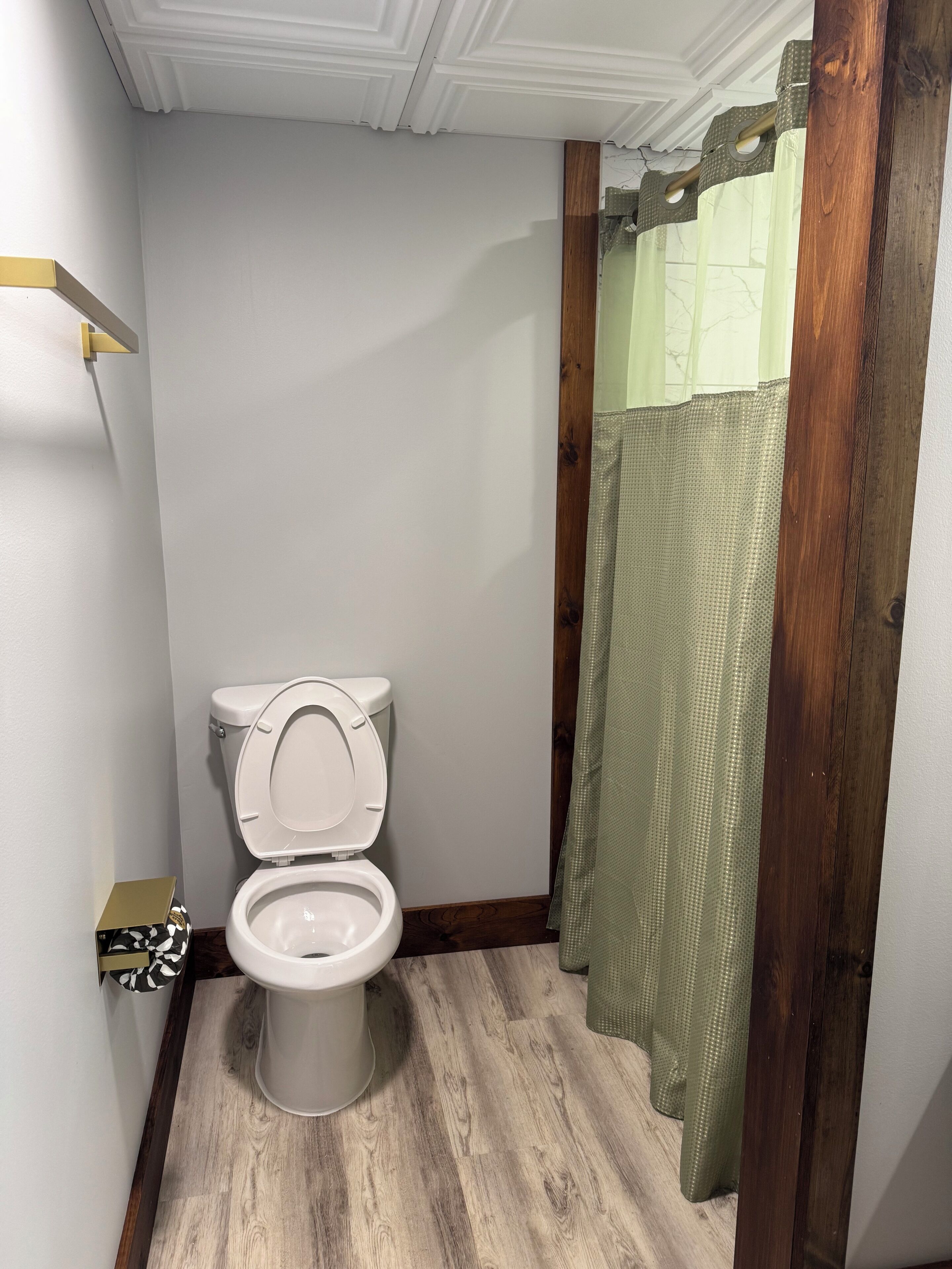 Un baño con inodoro, suelo de madera, pared blanca y cortina de ducha verde.