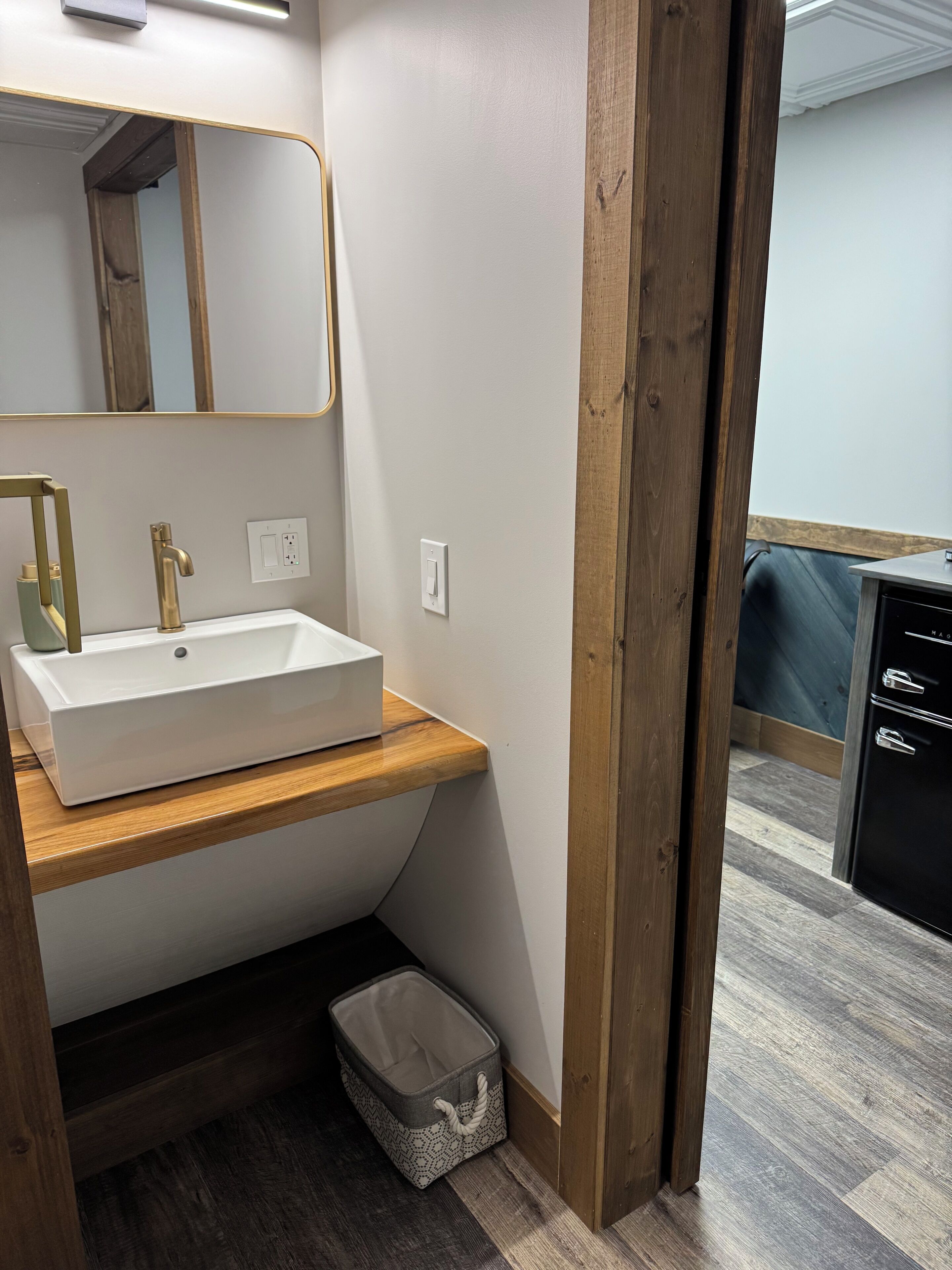 A modern bathroom with a white sink, gold faucet, and a wooden vanity.