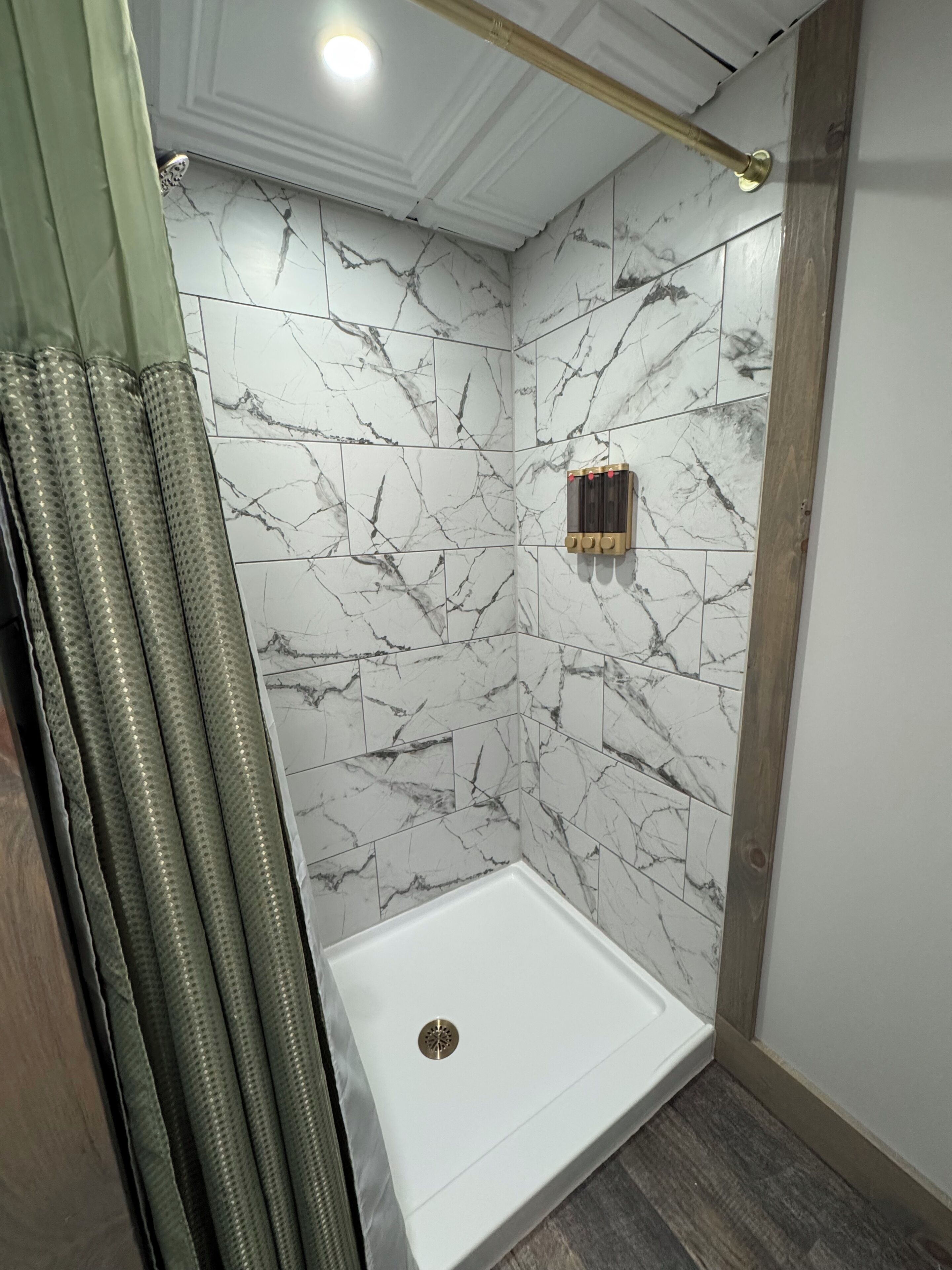 Une douche aux murs de marbre, une baignoire blanche et un plancher en bois.