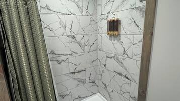 Une douche aux murs de marbre, une baignoire blanche et un plancher en bois.