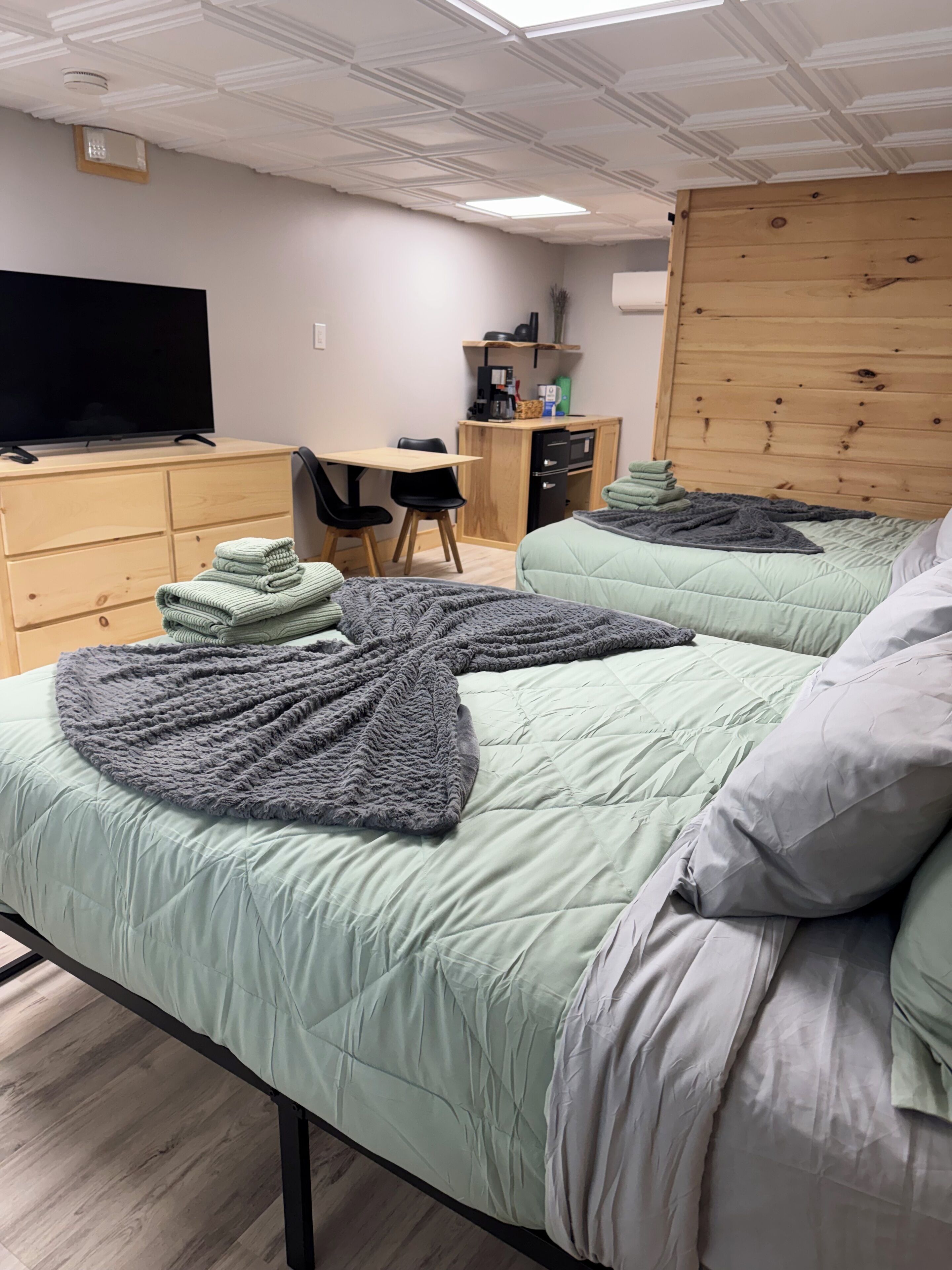 A room with two beds, a desk, a television, and a wooden headboard.