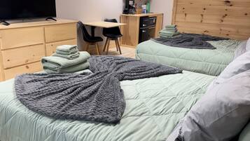 A room with two beds, a desk, a television, and a wooden headboard.