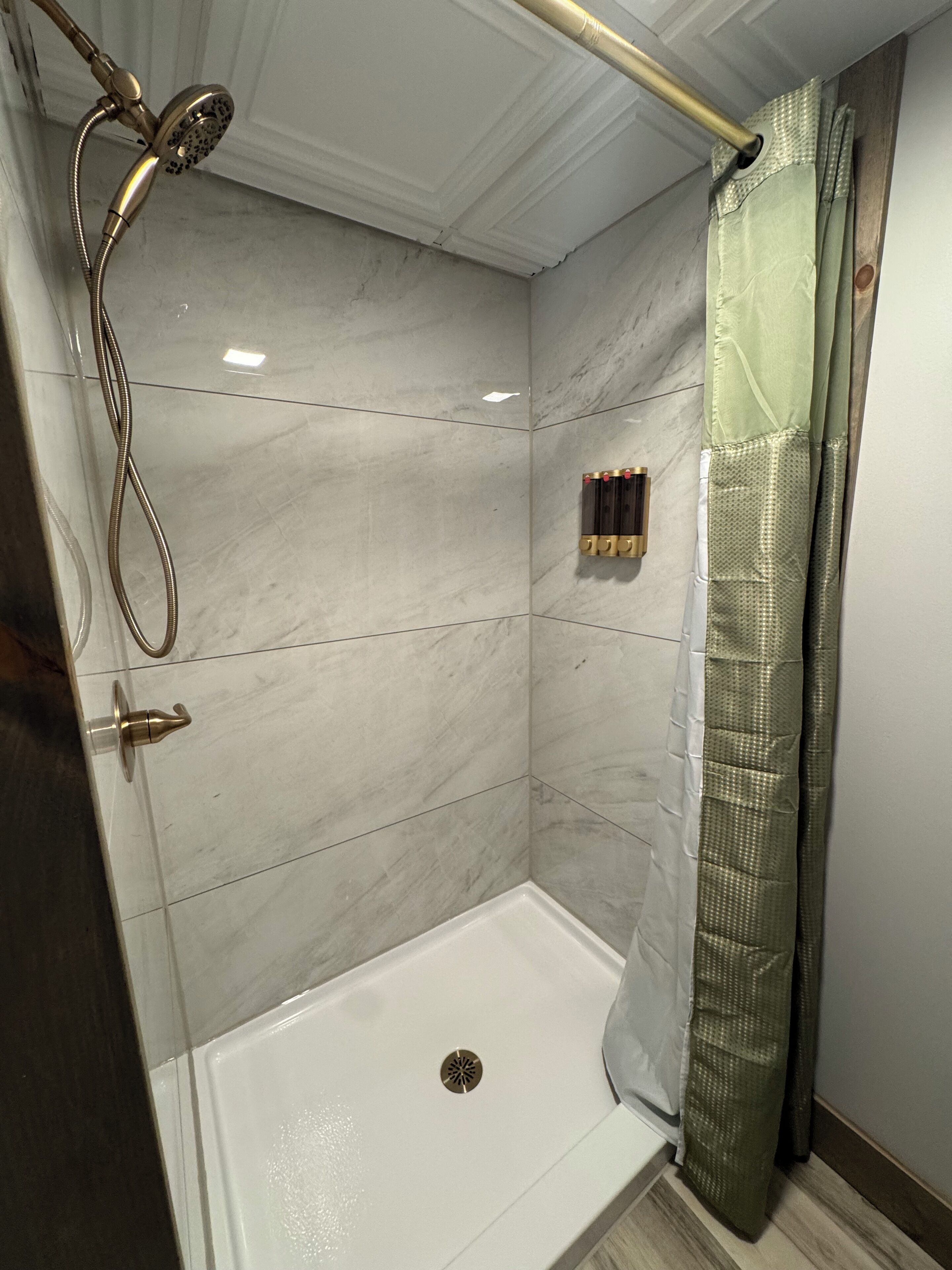 A shower with a handheld showerhead, a glass door, and a shower curtain.
