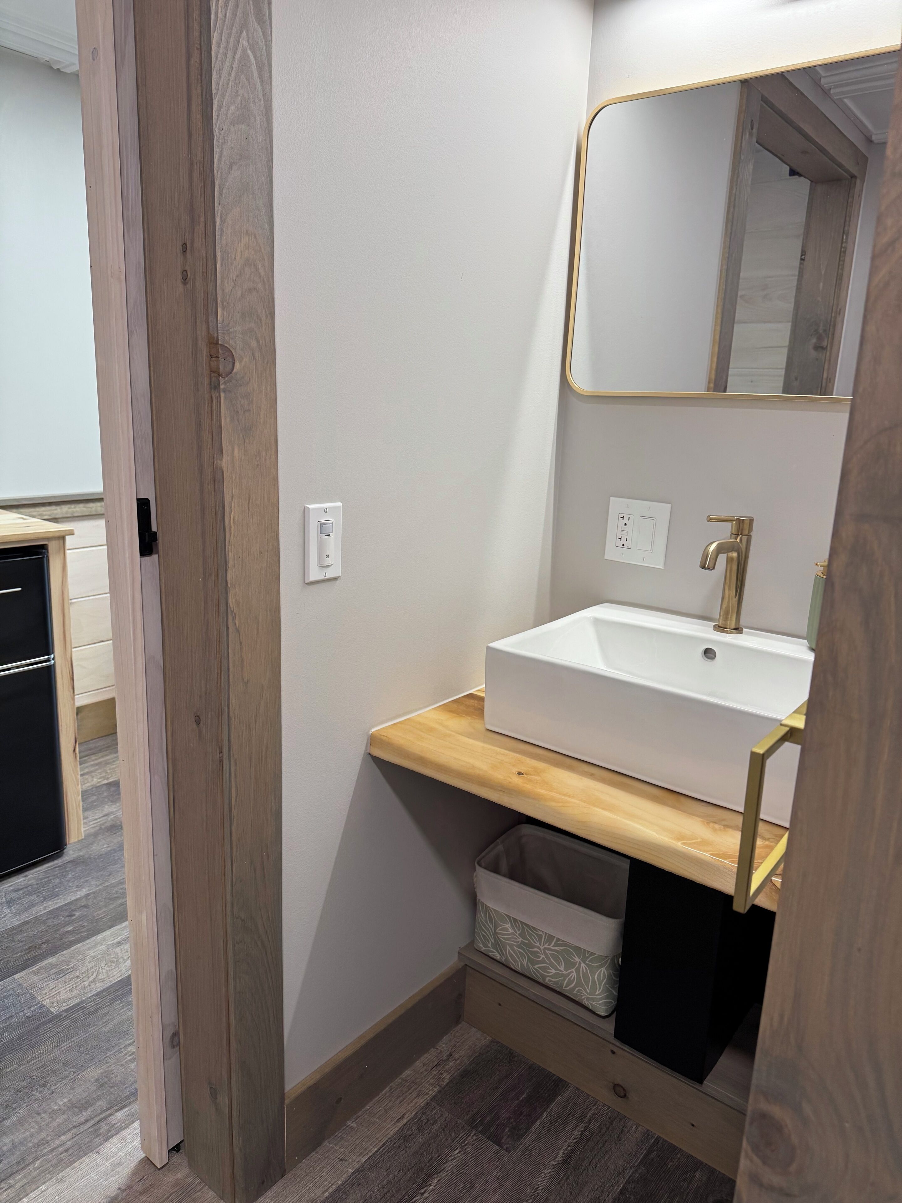 A bathroom with a wooden vanity, white sink, and a mirror.