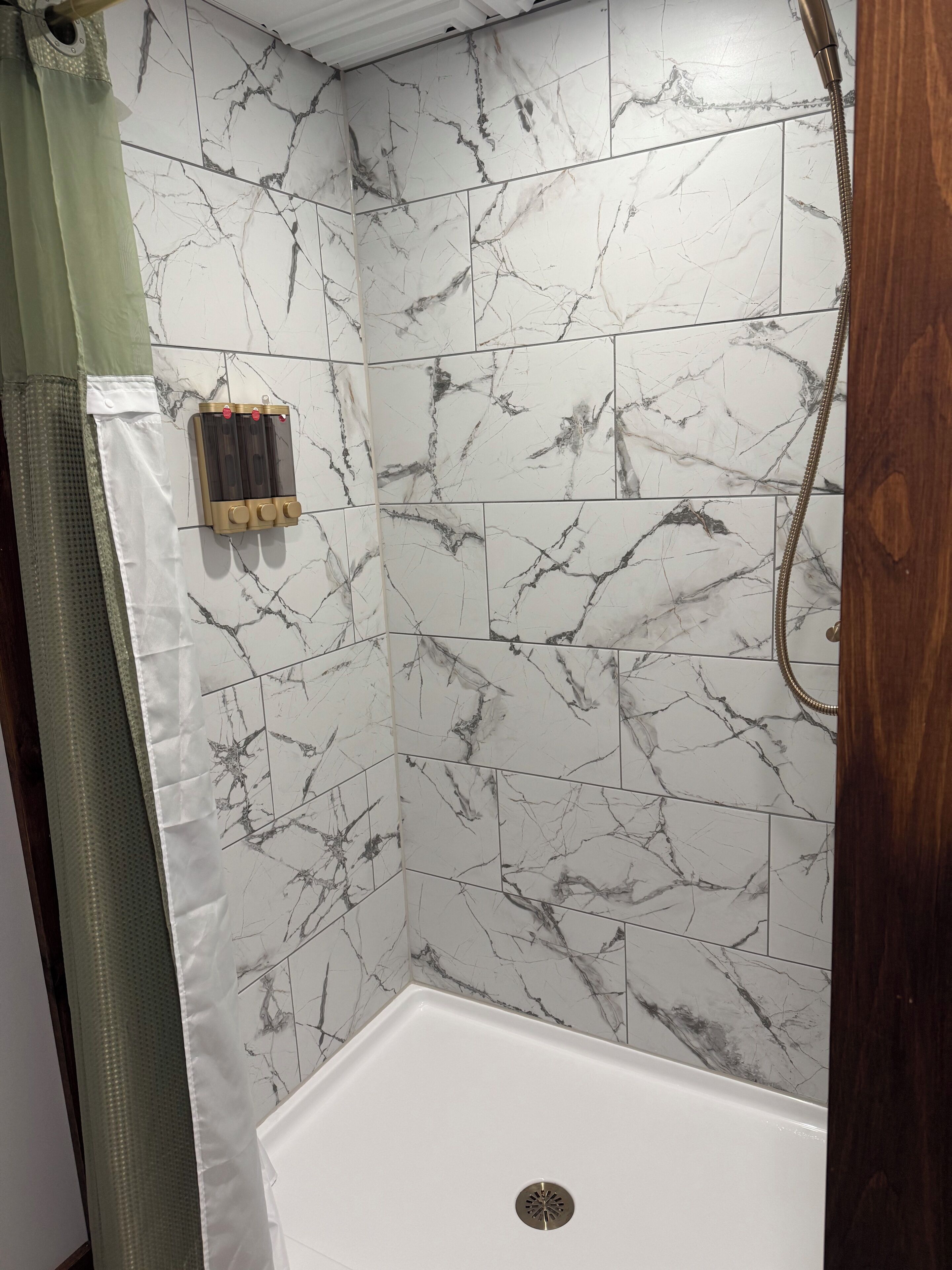 Un espace douche avec des carreaux de marbre blanc, une pomme de douche et un panneau de commande.