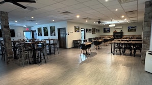 A spacious restaurant with multiple tables and chairs, a ceiling fan, and a stone pillar.
