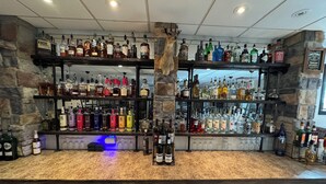 A bar area with shelves of liquor bottles, a decorative animal head, and a refrigerator with bottles.