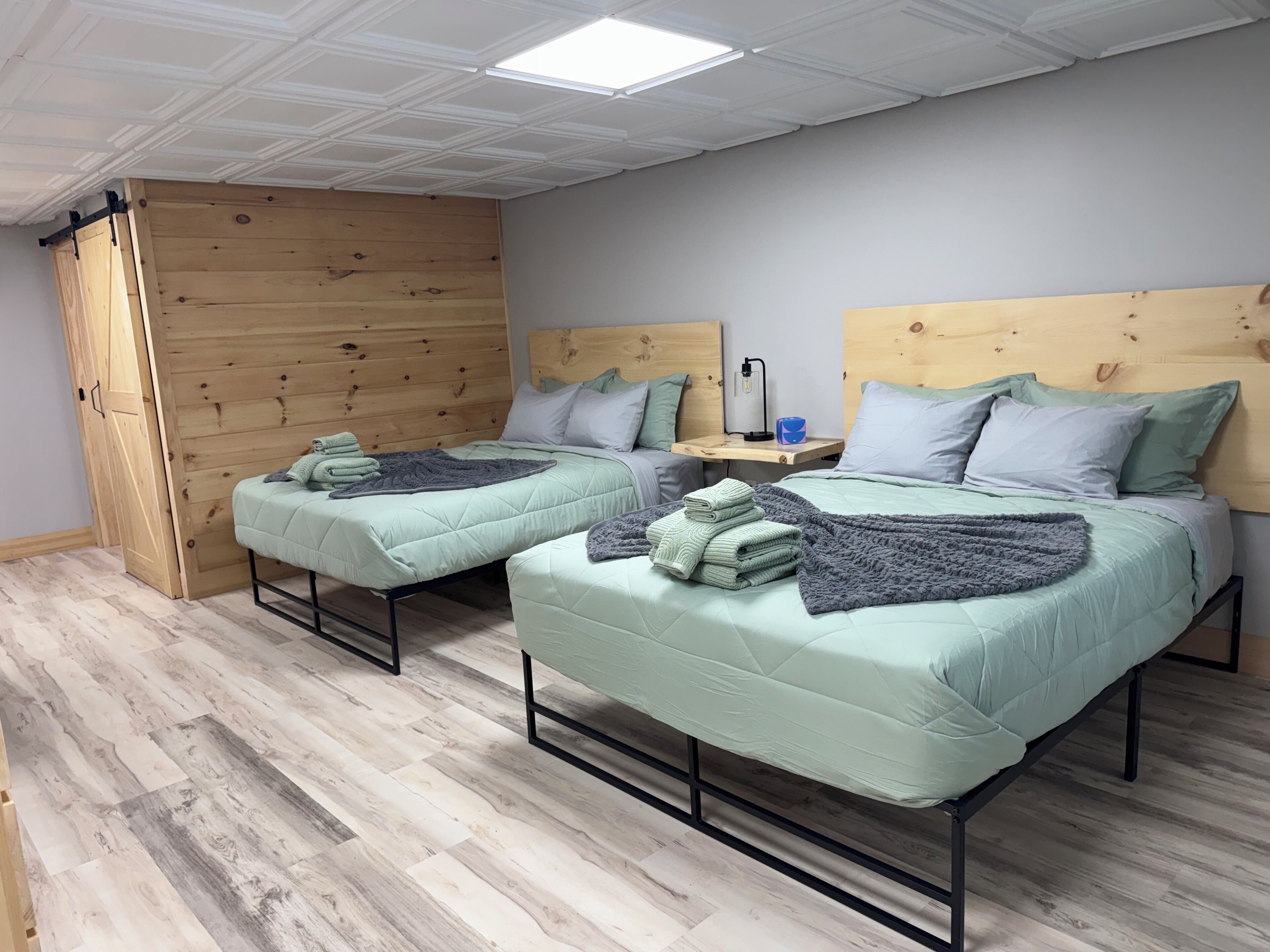 A room with two beds, a wooden wardrobe, a desk with a lamp, and a ceiling light.