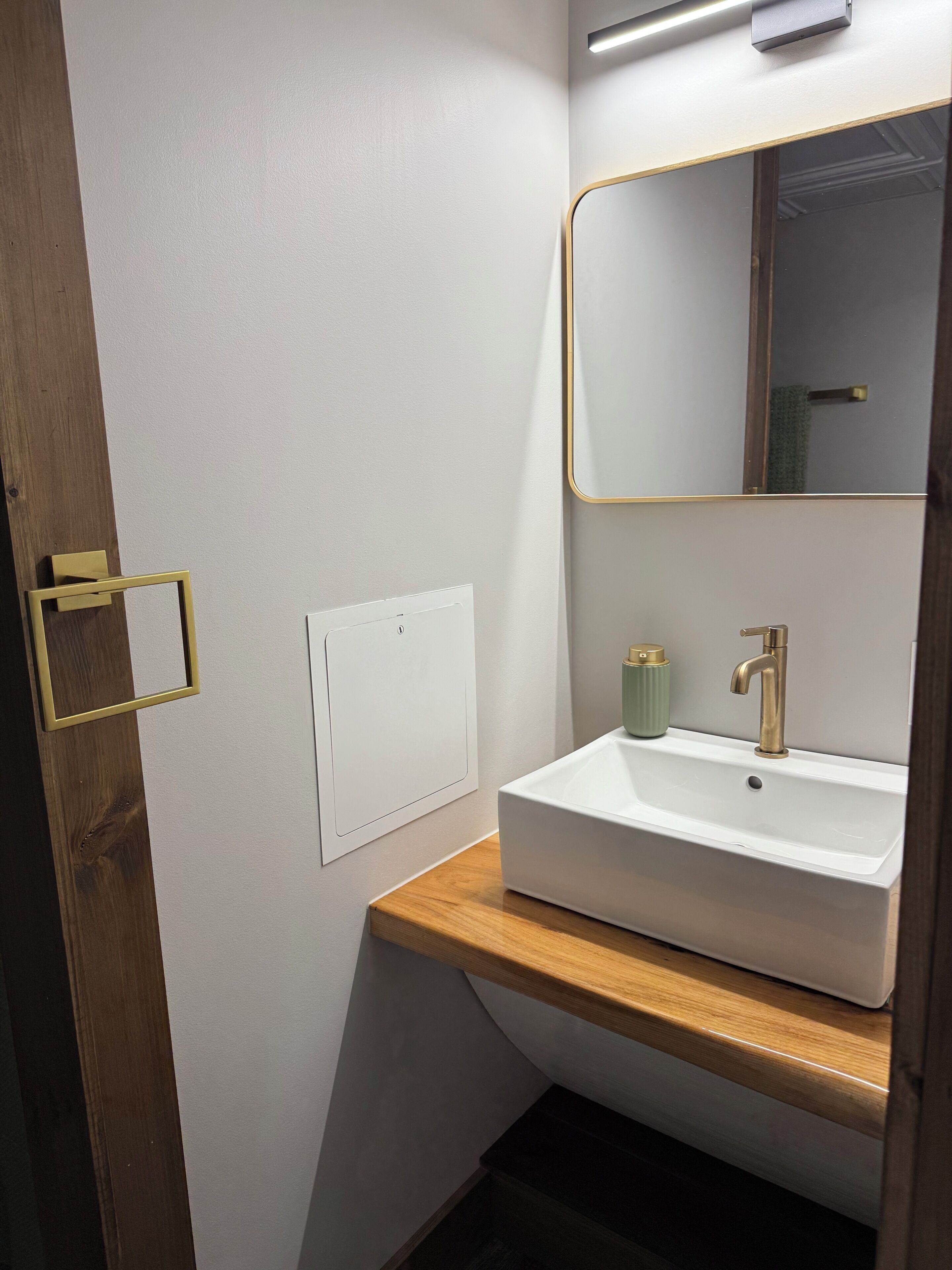 Een badkamer met een wit wastafel, een spiegel met gouden lijst en een houten aanrecht.