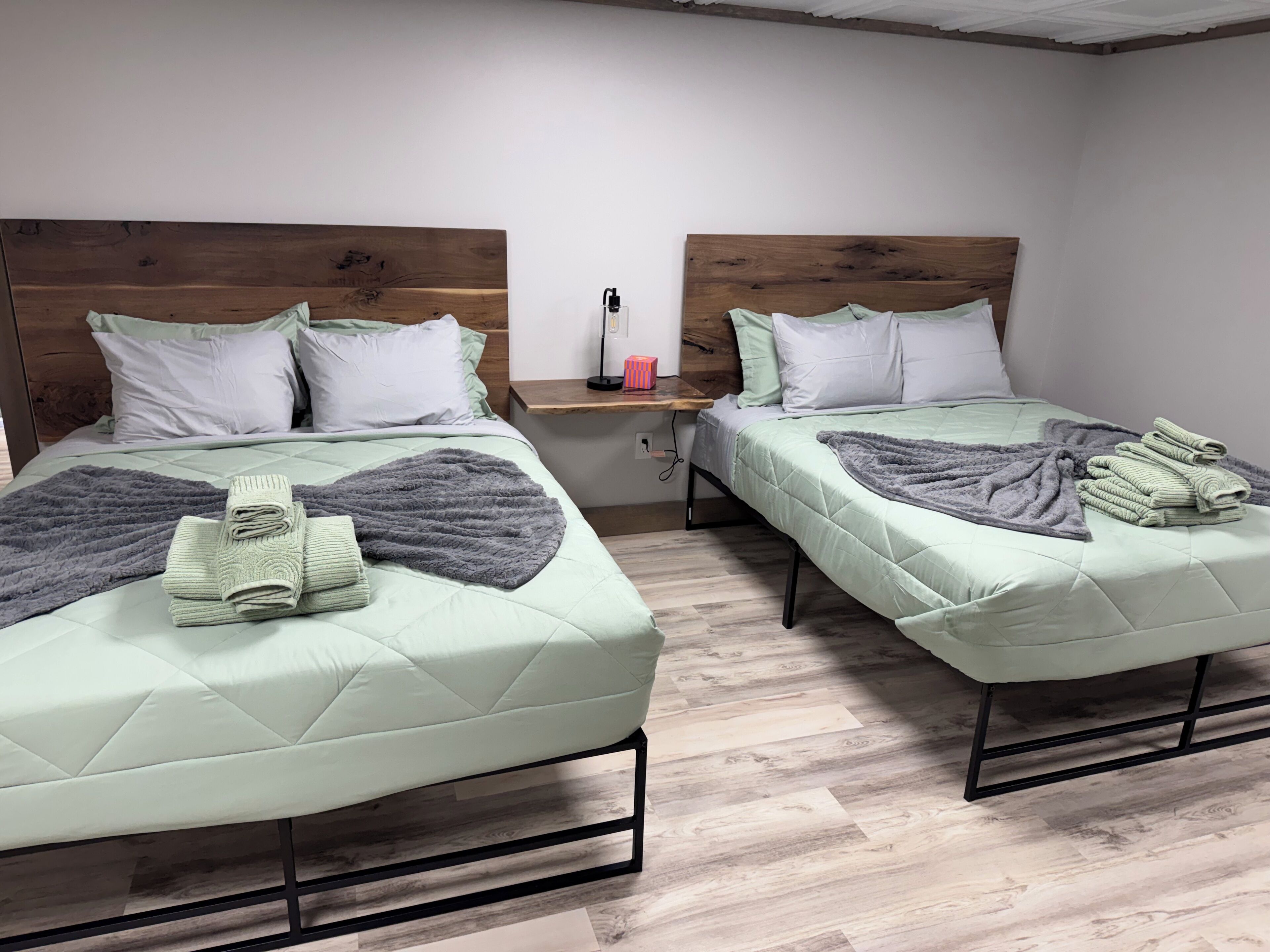 Two twin beds with wooden headboards, a bedside table with a lamp, and a folded towel on each bed.