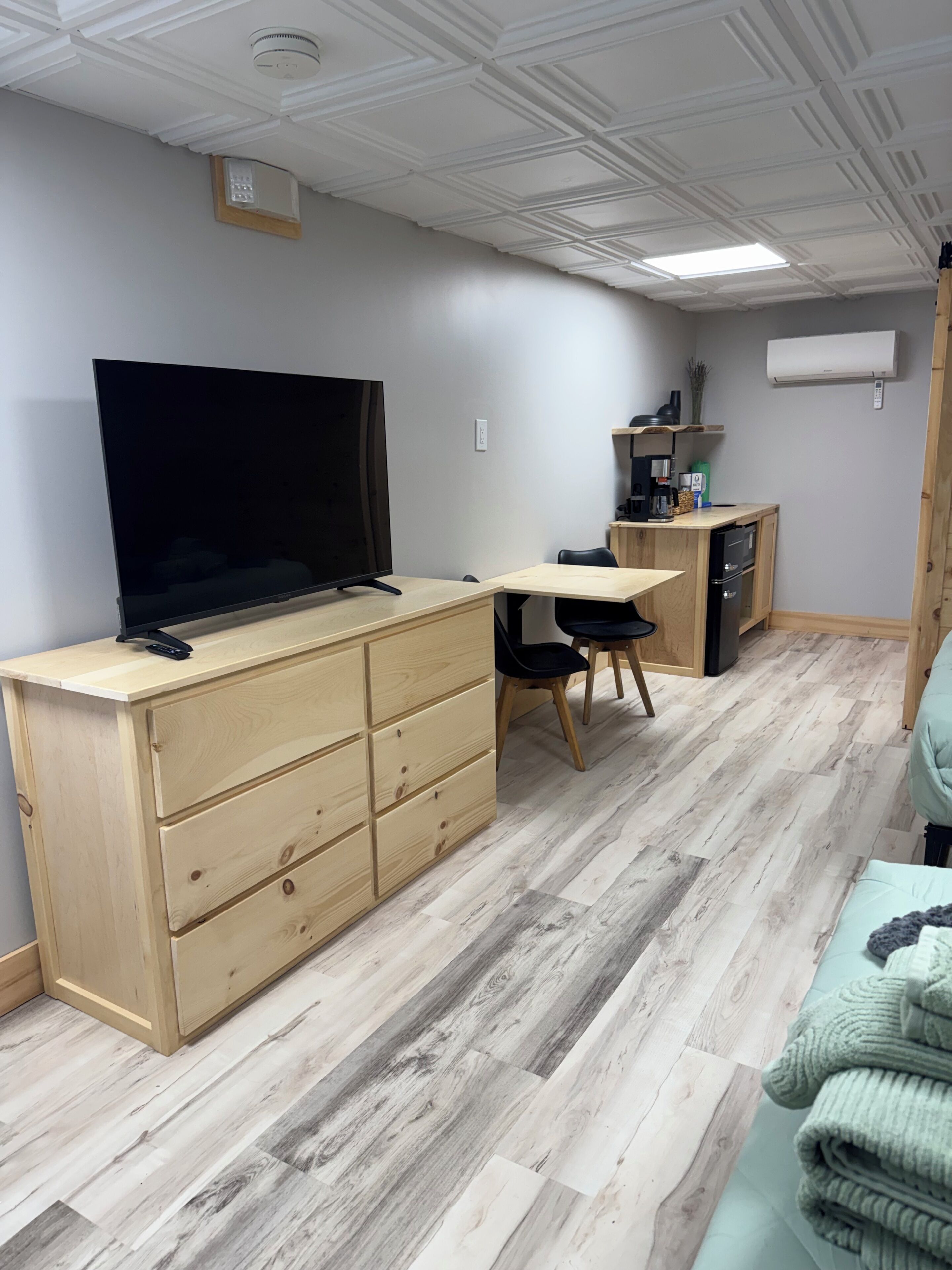 A compact living space with a TV, wooden furniture, a small kitchenette, and a ceiling with recessed lighting.