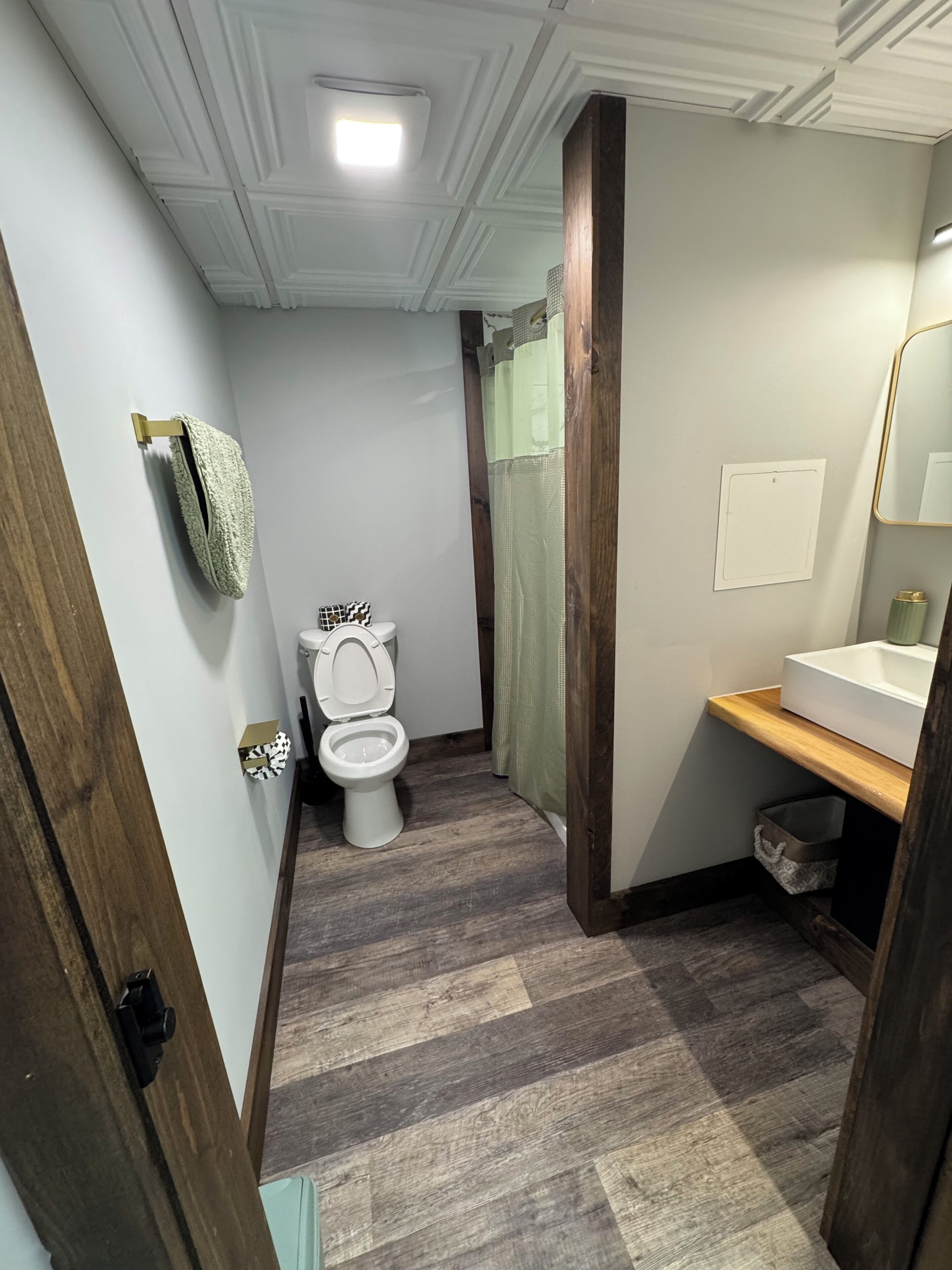 Une salle de bain équipée de toilettes, d’un rideau de douche et d’un meuble-lavabo en bois avec un miroir.