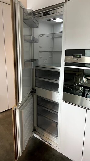 A commercial kitchen with stainless steel appliances, including a refrigerator, oven, and a digital clock displaying 1:30. - 1 bed sub penthouse in Chinatown/Stadium (Vancouver)