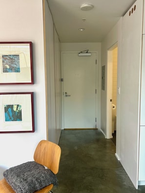A hallway with a door, a framed picture on the wall, and a chair with a cushion. - 1 bed sub penthouse in Chinatown/Stadium (Vancouver)