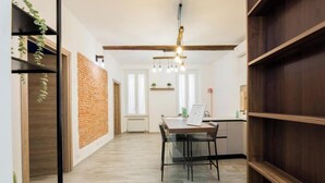 A modern interior with a brick wall, wooden beams, a dining area with a table and chairs, and a hanging light fixture. - Aquarium 3' | 2BR | A/C | Wifi & Netflix by Tilo (Genoa)