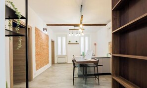 Ein modernes Interieur mit Backsteinwand, Holzbalken, einer Essecke mit Tisch und Stühlen sowie einer hängenden Leuchte.