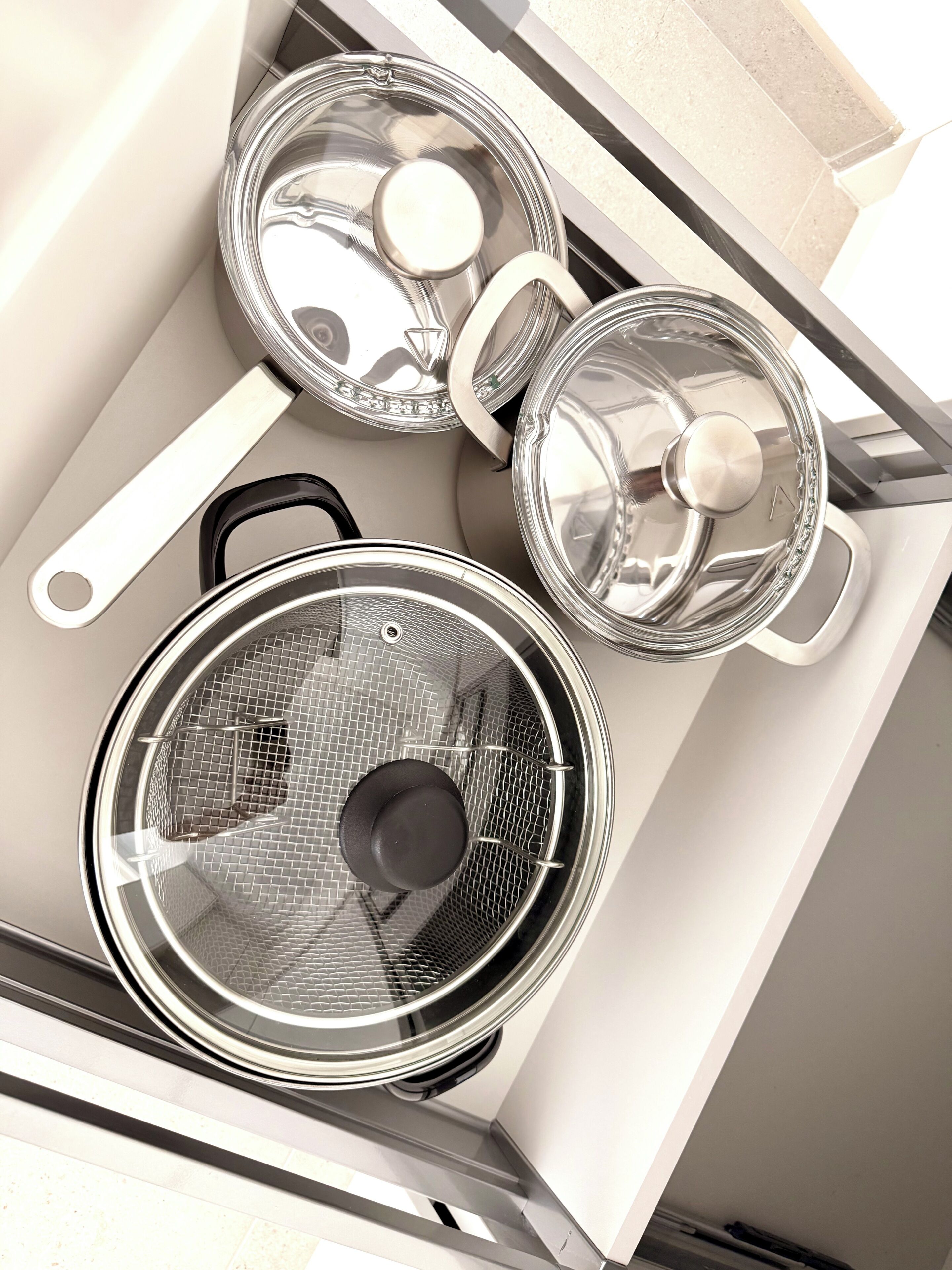 A kitchen with three stainless steel pots and a black pan on a white countertop.