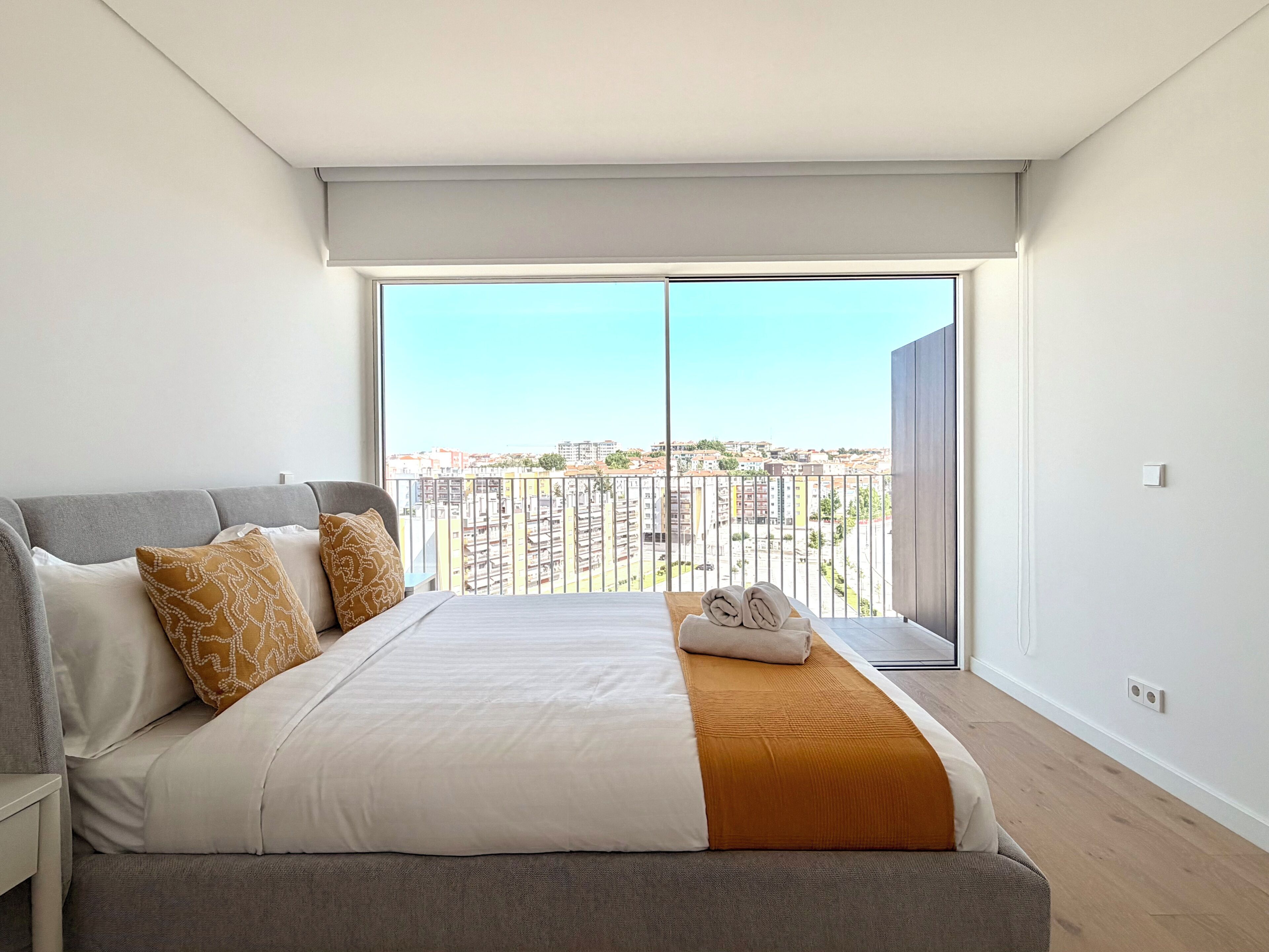 A bedroom with a large bed, a view of the city through a balcony, and a modern design.