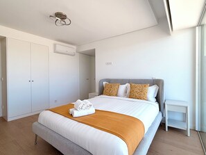 A modern bedroom with a large bed, a wardrobe, a bedside table, and a ceiling light fixture. - Barreiro Nooba 263C Apartment BY LULUNA (Barreiro)