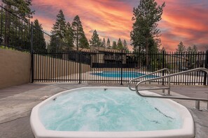 Ein Whirlpool mit Blick auf ein Schwimmbecken und Bäume, umzäunt.