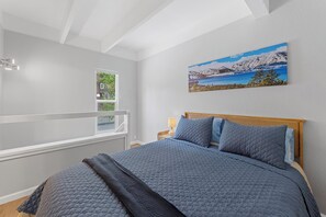 Ein Schlafzimmer mit Bett, Fenster, Gemälde und Nachttisch.