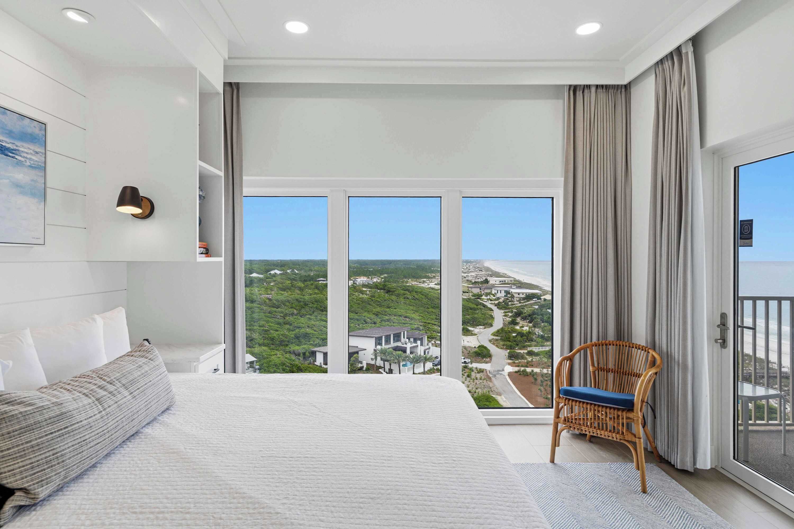 Habitación de hotel con una cama grande, una silla de mimbre, vistas del paisaje y un balcón.