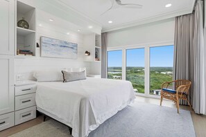Ein Schlafzimmer mit einem großen Bett, einem Sessel, einem Bücherregal und Blick ins Freie.