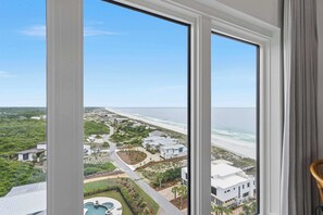 Ein Hotelzimmer in einem Hochhaus mit großem Fenster, Blick auf einen Strand und einen Golfplatz.