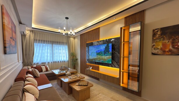 Una sala de estar moderna con un televisor de pantalla plana grande, un sofá, una mesa de centro y una planta decorativa.