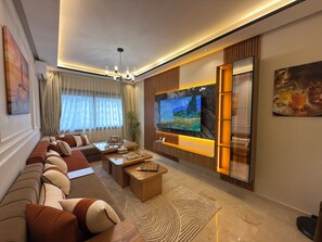 A modern living room with a large flat-screen TV, a sofa, a coffee table, and a decorative plant. - Sanctuaire Soleil & Luxe Casablanca (Casablanca)