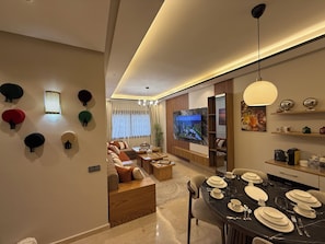 A modern living room with a sofa set, a dining table set for four, and a TV mounted on the wall.