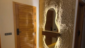 Una habitación con puerta de madera, pared de piedra con arco tallado y un banco acolchado blanco.
