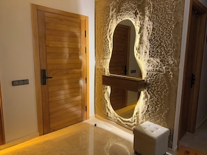 A room with a wooden door, a stone wall with a carved arch, and a white cushioned bench.