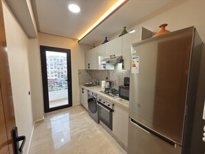 A modern kitchen with stainless steel appliances, a granite countertop, and a view of the city through a large window.