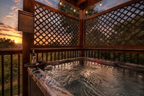 Ein Whirlpool mit Holzterrasse und Sicherheitshinweis, umgeben von einem Gitterzaun und Bäumen.