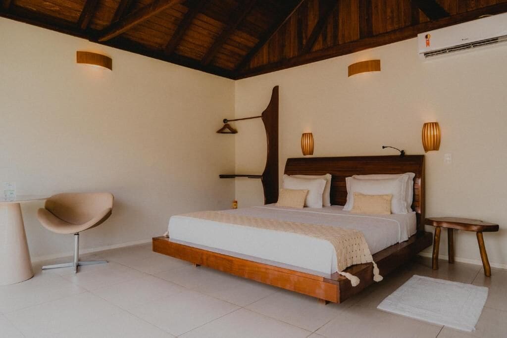 Un dormitorio con estructura de cama de madera, una silla, mesitas de noche y una lámpara colgante.